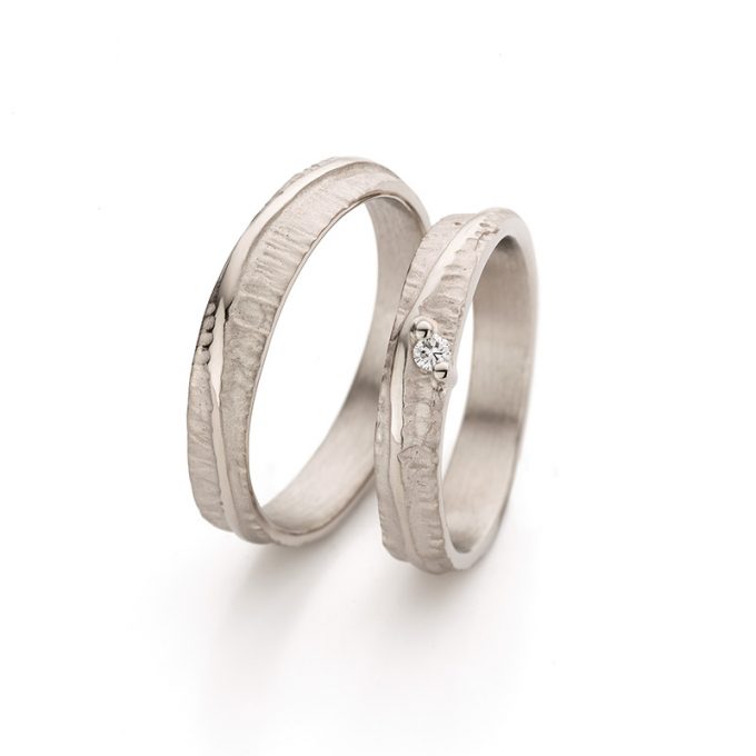 Refined white wedding rings with smooth details on a surface with a subtle relief and a diamond on the ring for ladies.